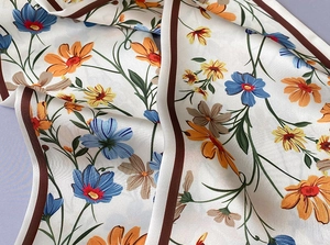 Detalle de bufanda de satén con estampado floral, margaritas coloridas y borde en contraste