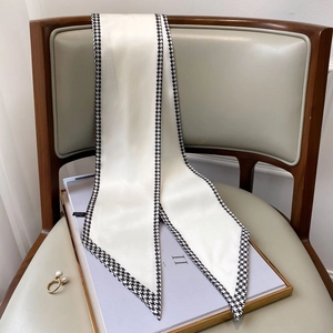 Detail of a white narrow silk scarf with houndstooth edges draped over a purple book