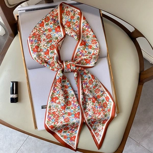 Pañuelo estrecho de seda con estampado floral anudado en lazo sobre una revista blanca