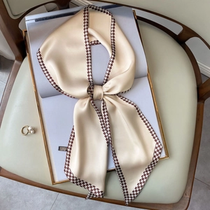 Elegant houndstooth silk scarf in beige, tied as a bow on a magazine backdrop