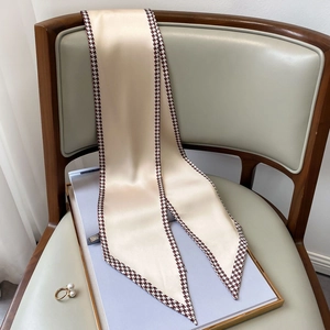 Detail of champagne satin skinny scarf with houndstooth edge draped on a chair