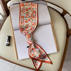 Primer plano de un pañuelo de seda estrecho con flores y borde rojo sobre un libro
