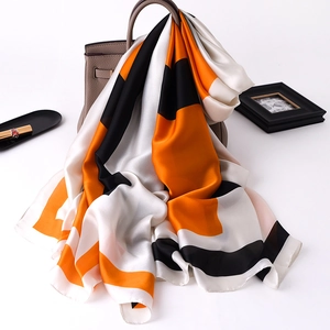 Silk-like satin scarf with orange and black geometric blocks draped over a handbag