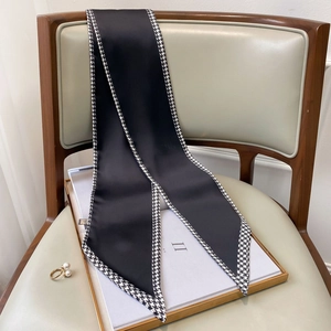 Detailed view of black silk twilly scarf with houndstooth trim on a stylish chair