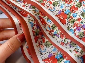 Primer plano de bufanda de seda con flores mostrando caída suave y bordes de rayas