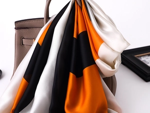 Close-up of silk scarf with orange and black blocks tied on a beige leather handbag
