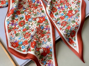 Detalle de bufanda de seda con estampado floral, textura suave y finos bordes rojos