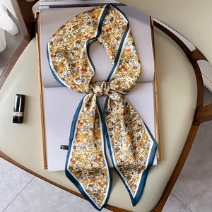 Pañuelo estrecho de seda con estampado floral y borde azul sobre un sillón de cuero