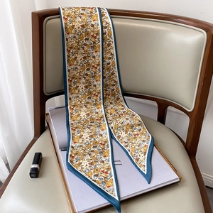 Detalle de bufanda estrecha de seda floral sobre una silla con accesorios elegantes