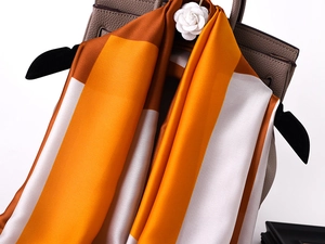 Detail of silk scarf with orange and brown blocks draped on a leather handbag
