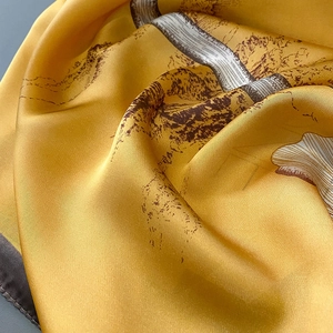 Detailed texture of golden satin scarf featuring vintage mountain landscape line art
