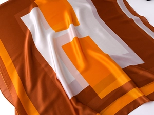 Detailed close-up of glossy silk-feel scarf with orange and brown H-letter patterns