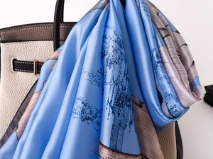 Close-up of lightweight lake blue silk scarf with artistic tree print on a leather handbag