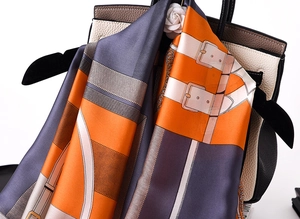 Detailed view of luxury silk scarf with chain pattern draped over a leather bag