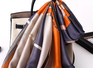Detail of luxury silk scarf with chain pattern tied on a leather handbag handle