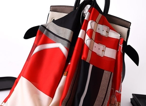 Detail of silk scarf with red and black leather belt pattern draped on handbag