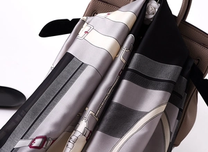Equestrian chain print silk scarf draped over a tan leather bag with camellia floral accent