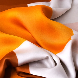Elegant silk-like scarf with orange and brown geometric patterns and smooth texture