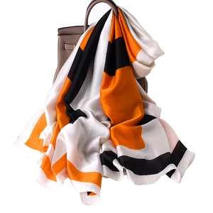 Elegant geometric silk scarf in orange and black draped on a stylish leather handbag