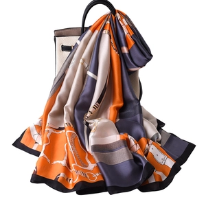 Elegant chain pattern silk scarf in orange and grey draped on a stylish handbag