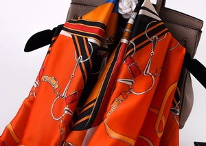 Detail of a silk scarf with equestrian patterns draped over a textured handbag