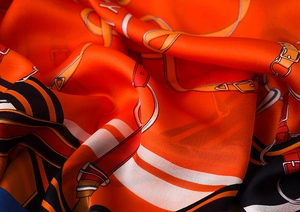 Detail of silk scarf with orange equestrian pattern and smooth glossy fabric texture
