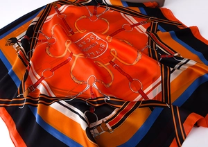 Detailed view of luxury silk scarf with orange equestrian pattern and smooth texture
