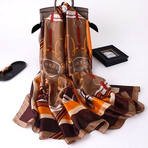 Detail of silk-like scarf with equestrian strap prints draped over a stylish handbag