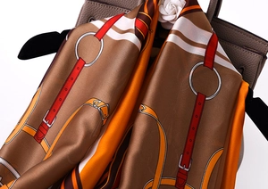 Detailed view of luxury silk scarf with orange horse harness print on leather bag