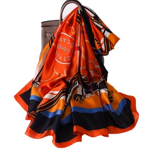 Satin silk scarf with horse and belt pattern draped on handbag in bright orange and blue