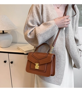 Brown textured leather crossbody bag with gold buckle shown in a lifestyle indoor setting