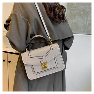 Detail of elegant beige crossbody bag with gold buckle on a brown trench coat outfit