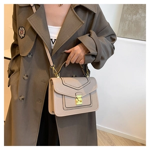 Detail of beige square crossbody bag with gold twist lock on a brown trench coat