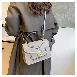 Detail view of taupe leather crossbody bag with gold clasp shown on person