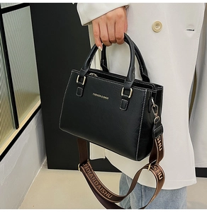 Detail of black leather handbag with gold lettering and adjustable wide strap