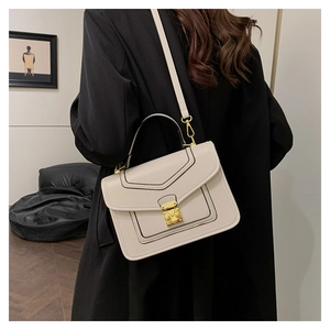Detail of a chic cream crossbody bag with a gold clasp worn by a model in a black coat