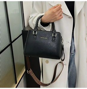 Detail of black vintage faux leather tote bag with wide woven strap and gold metal hardware