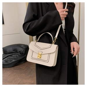 Detail of cream flap handbag with gold clasp, top handle, and elegant black oil-edge finish