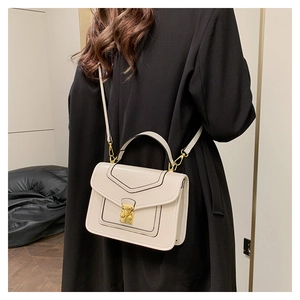 Detail of cream small square handbag with black trim and gold lock worn with a black coat