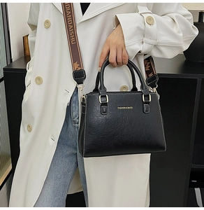 Detail of black pebbled leather tote with gold hardware and logo jacquard shoulder strap