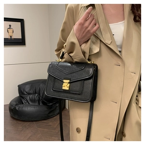 Detail of black lizard texture crossbody bag with gold buckle on a khaki trench coat