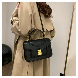 Close-up of structured black Saffiano leather crossbody bag with gold metal clasp detail