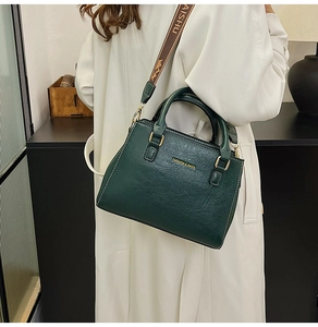 Detail of dark green textured leather tote bag with white stitching and woven strap