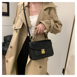 Detailed view of black lizard-textured crossbody bag with golden metal lock and strap