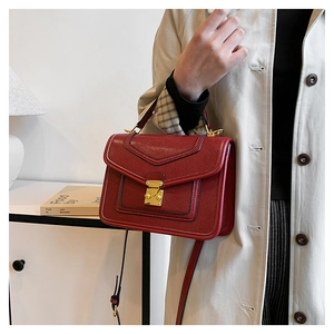 Detail of burgundy lychee grain leather handbag with gold metal clasp and top handle