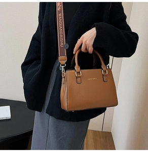 Close-up of brown leather tote bag with wide logo fabric strap and golden fashion text
