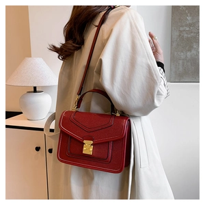 Detail of red textured leather bag with luxury gold buckle and structured flap design