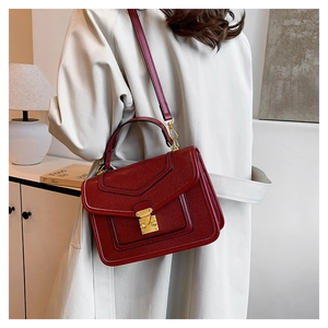 Close-up of red leather handbag with gold metal clasp and adjustable shoulder strap