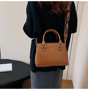 Brown leather tote bag with wide patterned shoulder strap shown in a lifestyle setting