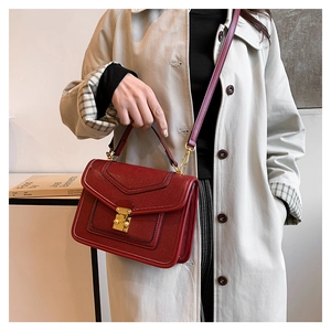 Detail of dark red lychee leather bag with gold metal lock on beige trench coat